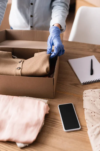 Partial view of seller in latex glove packing clothes into box in showroom — Stock Photo