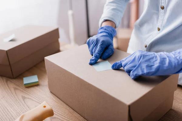 Partial view of showroom owner in latex gloves fixing sticky note on carton box — Stock Photo
