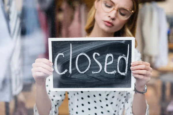 Displeased businesswoman holding board with closed lettering in showroom, blurred background — Stock Photo