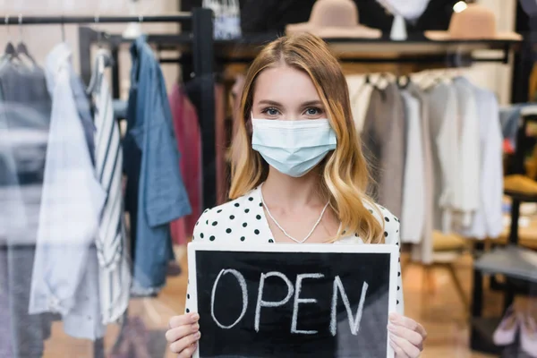 Positive businesswoman in medical mask, holding board with open lettering in showroom — Stock Photo