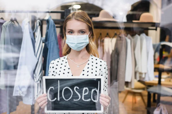 Showroom-Inhaberin mit medizinischer Maske, Blick auf Kamera und Haltetafel mit geschlossenem Schriftzug — Stockfoto