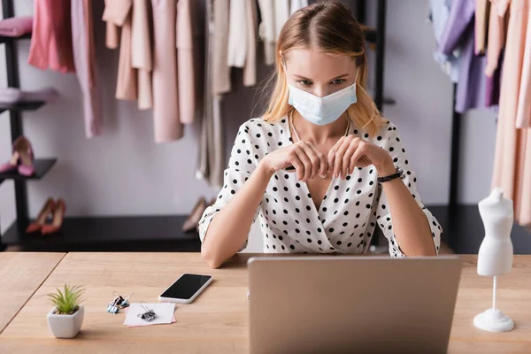 Showroom owner working near laptop and smartphone in medical mask — Stock Photo
