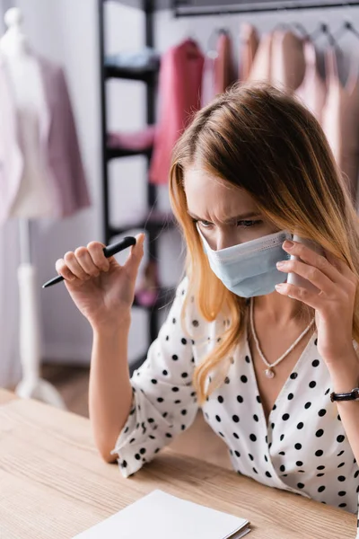 Propietario de sala de exposición serio aceptar orden en el teléfono móvil mientras trabaja en máscara médica - foto de stock