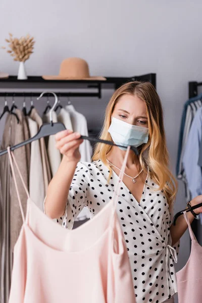 Showroom proprietário em máscara médica, segurando cabide com vestido em primeiro plano borrado — Fotografia de Stock