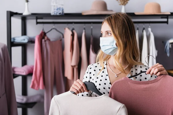 Propriétaire en masque médical, tenant des cintres et regardant loin dans le showroom — Photo de stock