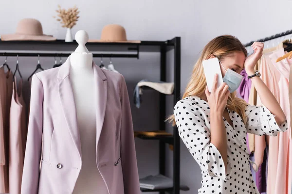 Upset businesswoman in medical mask talking on smartphone near mannequin — Stock Photo