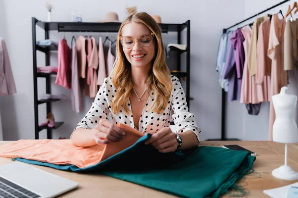 Smiling proprietor choosing samples of cloth at workplace in showroom, blurred foreground — Stock Photo