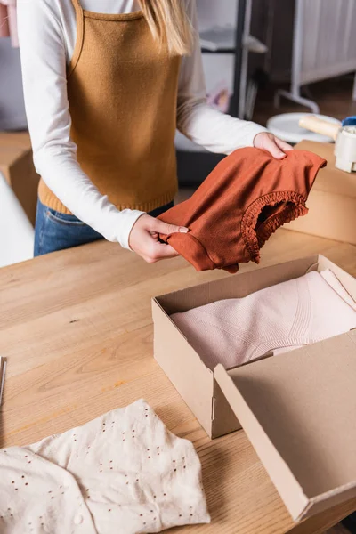 Partial view of proprietor holding sweater near box with clothing in showroom — Stock Photo