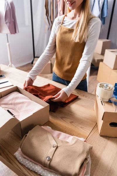 Partial view of smiling showroom owner packing clothes into carton box — Stock Photo