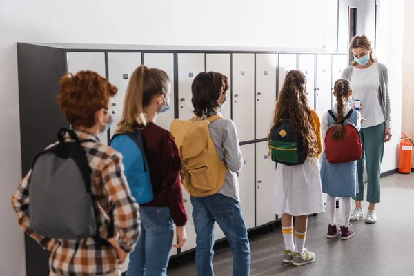 Schoolkids in medical masks standing in queue near teacher with infrared thermometer — Stock Photo