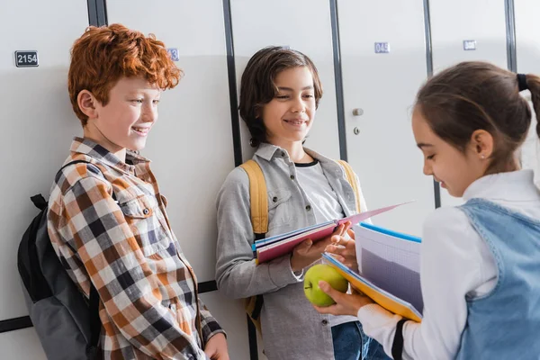 Écoliers joyeux regardant fille avec pomme et cahier sur le premier plan flou — Photo de stock