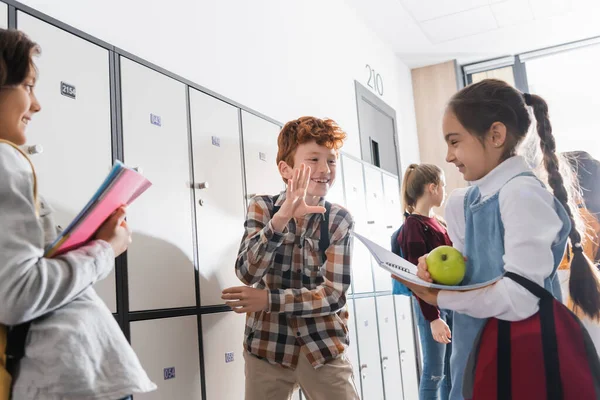 Studentessa positiva che parla con la studentessa con mela in mano e copybook su primo piano sfocato a scuola — Foto stock