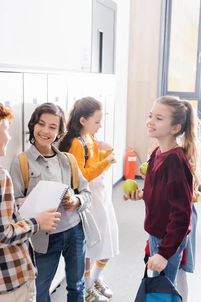 Smiling schoolchildren with ripe apples and notebook talking during brake in school — Stock Photo