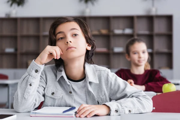 Pupil sitting near notebook and pen on desk — Stock Photo