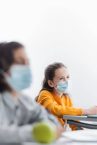 Chica en máscara médica cerca de compañero de clase en primer plano borrosa - foto de stock