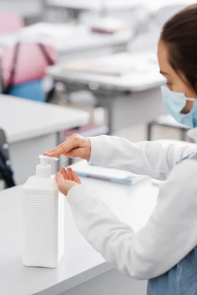 Cropped view of schoolgirl applying hand sanitizer in school on blurred foreground — Stock Photo