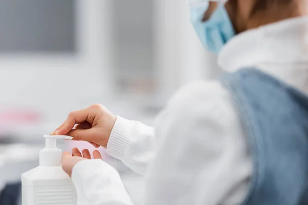 Cropped view of schoolgirl in medical mask applying hand sanitizer on blurred foreground — Stock Photo