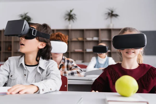 Amazed boy in vr headset looking away near pupils on blurred background — Stock Photo