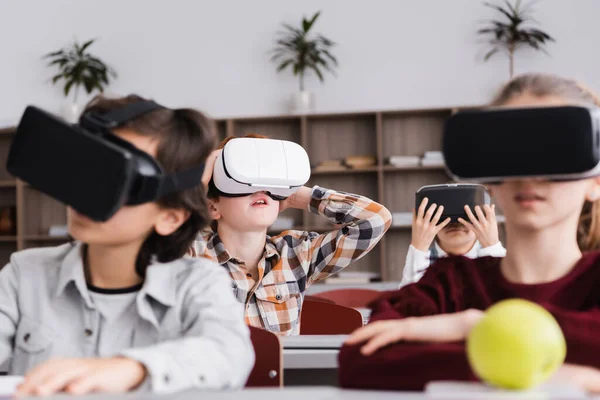 Избирательный фокус возбужденного школьника в наушниках vr возле учеников на размытом фоне — стоковое фото