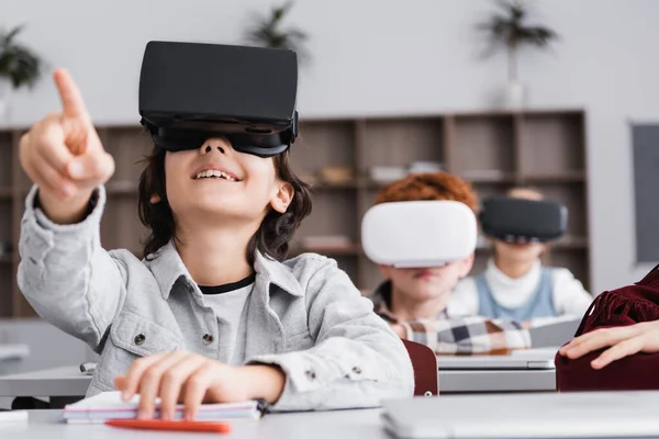 Joyful boy pointing with finger while gaming in vr headset, blurred background — Stock Photo