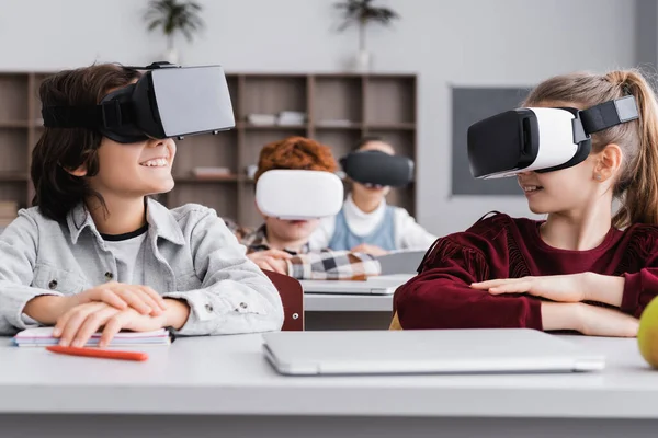 Happy classmates looking at each other while gaming in vr headsets in classroom — Stock Photo