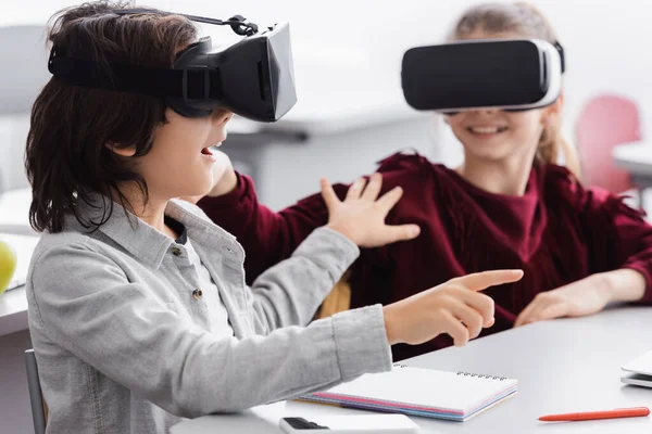Excited schoolboy touching classmate and pointing with finger while gaming in vr headset — Stock Photo