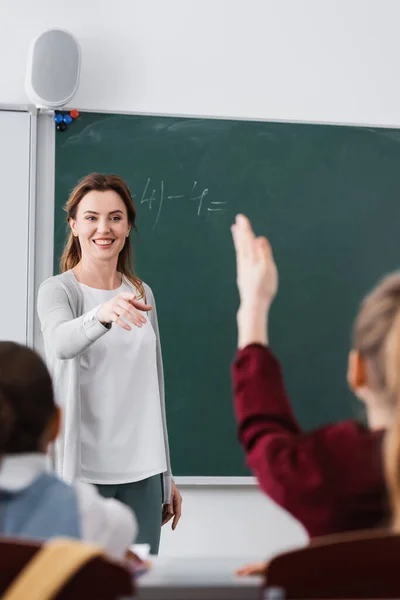 Feliz profesor señalando a colegiala levantando la mano en primer plano borrosa - foto de stock