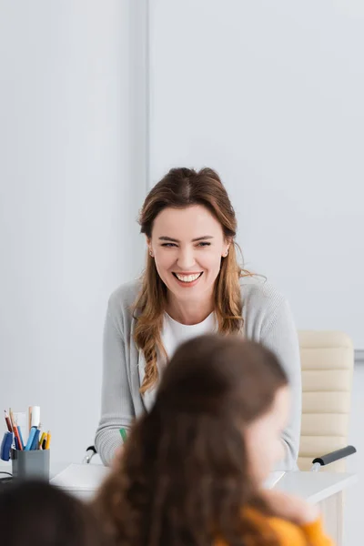 Взволнованный учитель смеется в классе на размытом переднем плане — стоковое фото