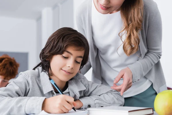 Teacher pointing with finger while helping schoolboy during lesson — Stock Photo