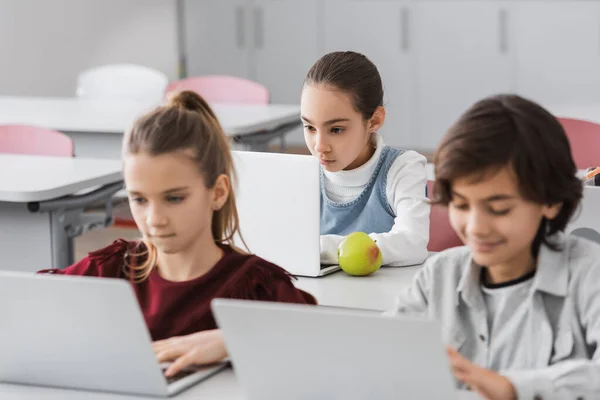 Concentrated schoolchildren using laptops in school on blurred foreground — Stock Photo