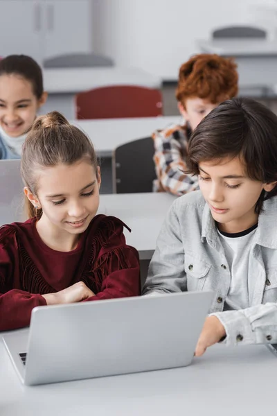 Escolares que usan ordenadores portátiles juntos durante la clase en la escuela - foto de stock