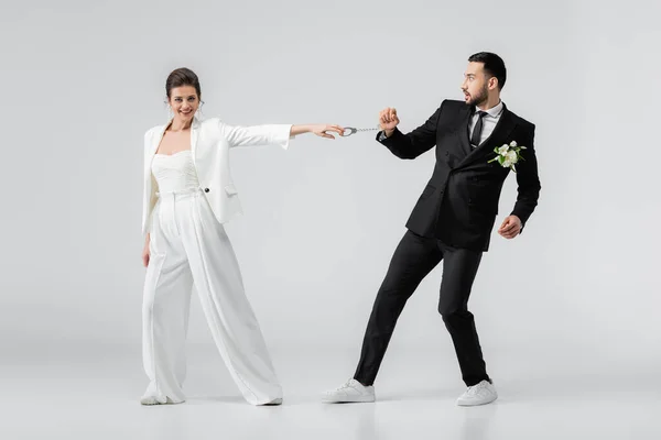 Positive Braut zieht Handschellen muslimischer Bräutigam auf weißem Hintergrund — Stockfoto