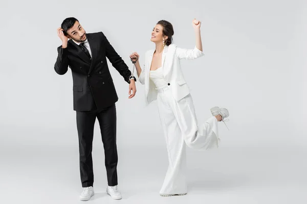 Glückliche Braut schaut nachdenklichen Bräutigam in Handschellen auf weißem Hintergrund an — Stockfoto