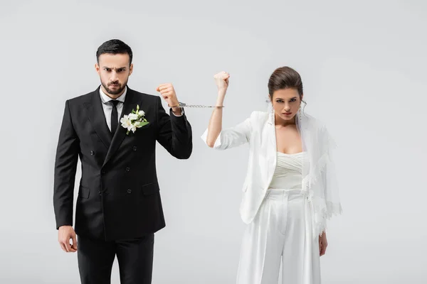 Angry multiethnic bride and groom in handcuffs looking at camera isolated on grey — Stock Photo