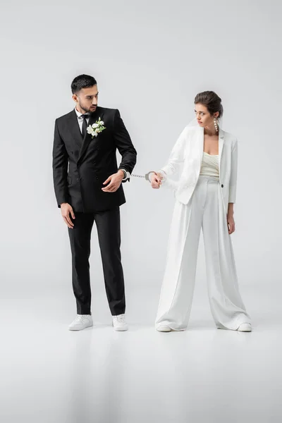Multiétnicos recém-casados algemados olhando uns para os outros no fundo branco — Fotografia de Stock