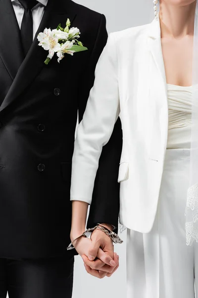 Vista recortada de la novia y el novio tomados de la mano con esposas aisladas en gris - foto de stock
