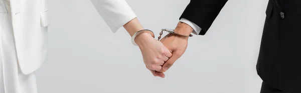 Cropped view of newlyweds holding hands in handcuffs isolated on grey, banner — Stock Photo