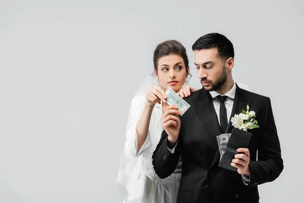 Muslim groom holding wallet and giving dollar banknote to bride isolated on grey — Stock Photo