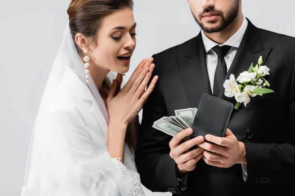 Mariée excitée regardant marié avec des dollars et portefeuille isolé sur gris — Photo de stock