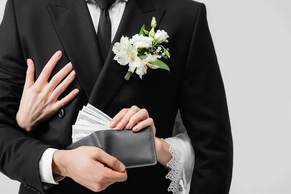 Vista recortada de la novia tomando dinero de la cartera en la mano del novio aislado en gris - foto de stock