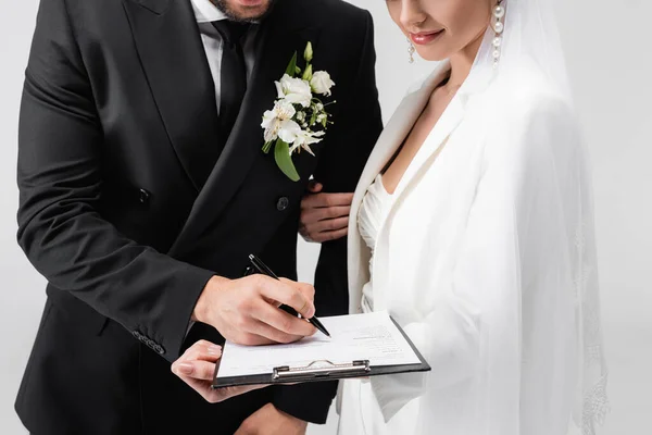 Vista cortada do contrato de assinatura do noivo perto da noiva em véu isolado em cinza — Fotografia de Stock