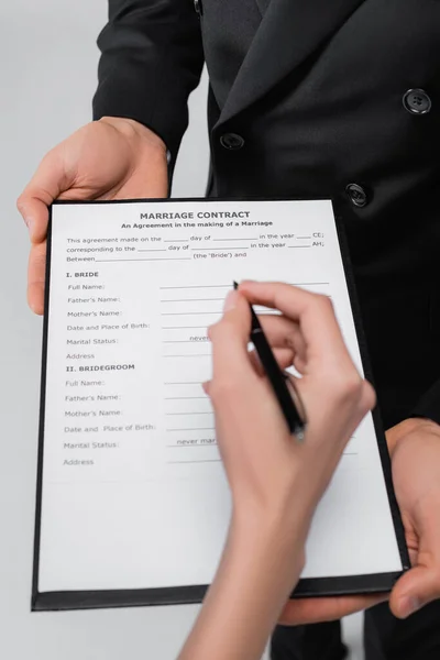 Cropped view of groom holding marriage contract near bride with pen isolated on grey — Stock Photo