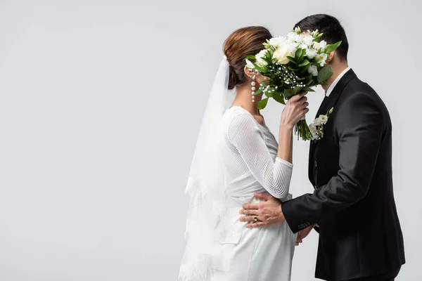 Mariée enceinte et marié se cachant derrière bouquet isolé sur gris — Photo de stock