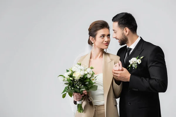 Elegante sposo arabo che tiene per mano felice giovane sposa isolata su grigio — Foto stock