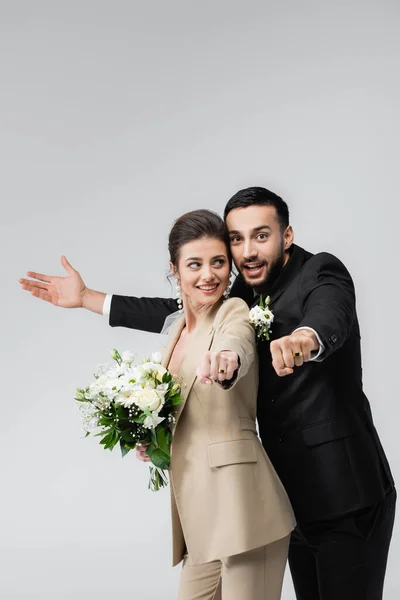 Excited, multiethnic newlywed couple showing wedding rings isolated on grey — Stock Photo