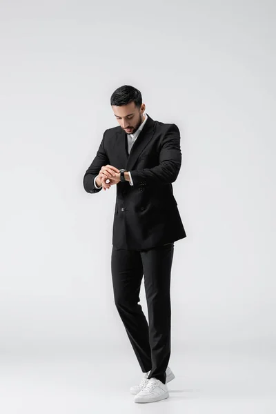 Vista a tutta lunghezza dell'uomo musulmano alla moda che controlla il tempo sull'orologio da polso su grigio — Foto stock