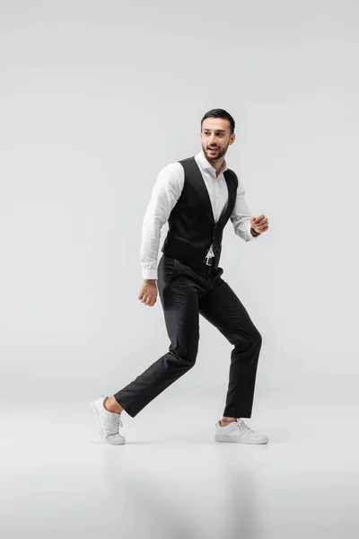 Full length view of smiling, trendy arabian man looking away while walking on grey — Stock Photo