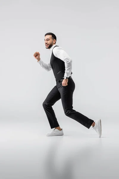 Vue pleine longueur de jeune homme arabe en vêtements à la mode et baskets fonctionnant sur gris — Photo de stock