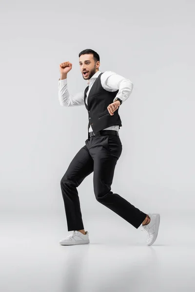 Full length view of excited arabian man in fashionable clothes dancing on grey — Stock Photo