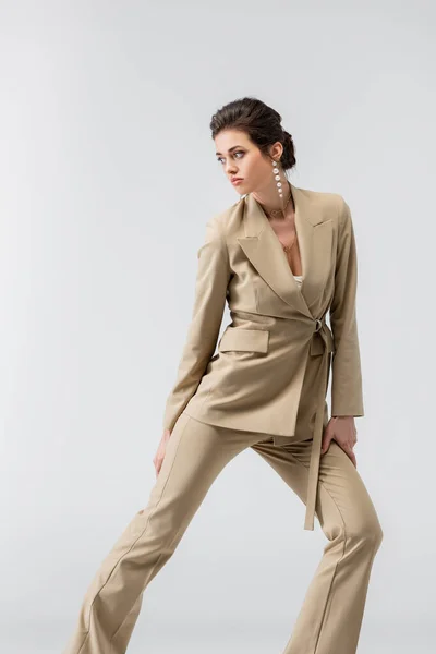 Bonita mujer en traje de pantalón de moda mirando hacia otro lado mientras posando aislado en gris - foto de stock